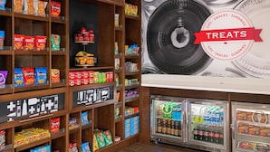 A snack display with various chips and snacks, a refrigerated section with beverages, and a wall with a large plate design. - Hampton Inn & Suites Pittsburgh New Stanton (New Stanton)