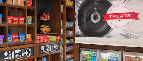 A snack display with various chips and snacks, a refrigerated section with beverages, and a wall with a large plate design.