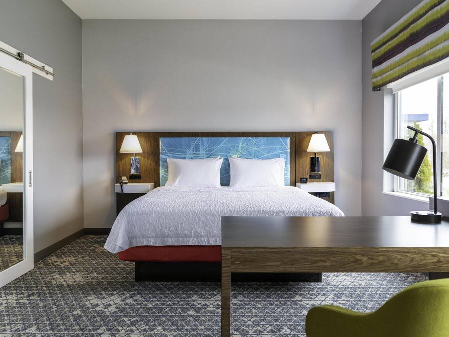 Una habitación de hotel con cama, lámparas de noche, escritorio y ventana con cortinas.
