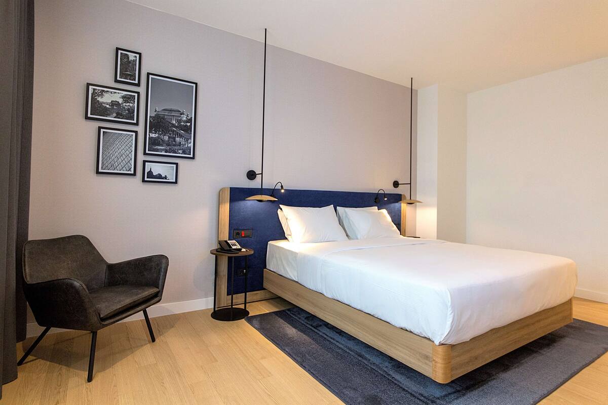 A modern hotel room with a large bed, a chair, and framed pictures on the wall.