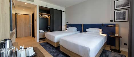 A hotel room with two beds, a desk with a tray of breakfast items, and a walk-in closet.