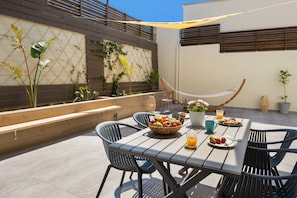 An outdoor patio with a wooden table, black chairs, a hammock, and a variety of fruits and drinks. - E & G Relax Homes (Kissamos)