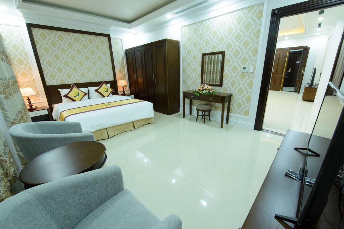 Ein Hotelzimmer mit einem Bett, zwei Sesseln, einem Schreibtisch mit Spiegel und einem Kleiderschrank.