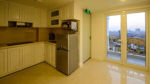 A kitchen with white cabinets, a stainless steel refrigerator, and a microwave. There is a balcony with a view of the city. - The Shine Office and Apartment (Hai Phong)