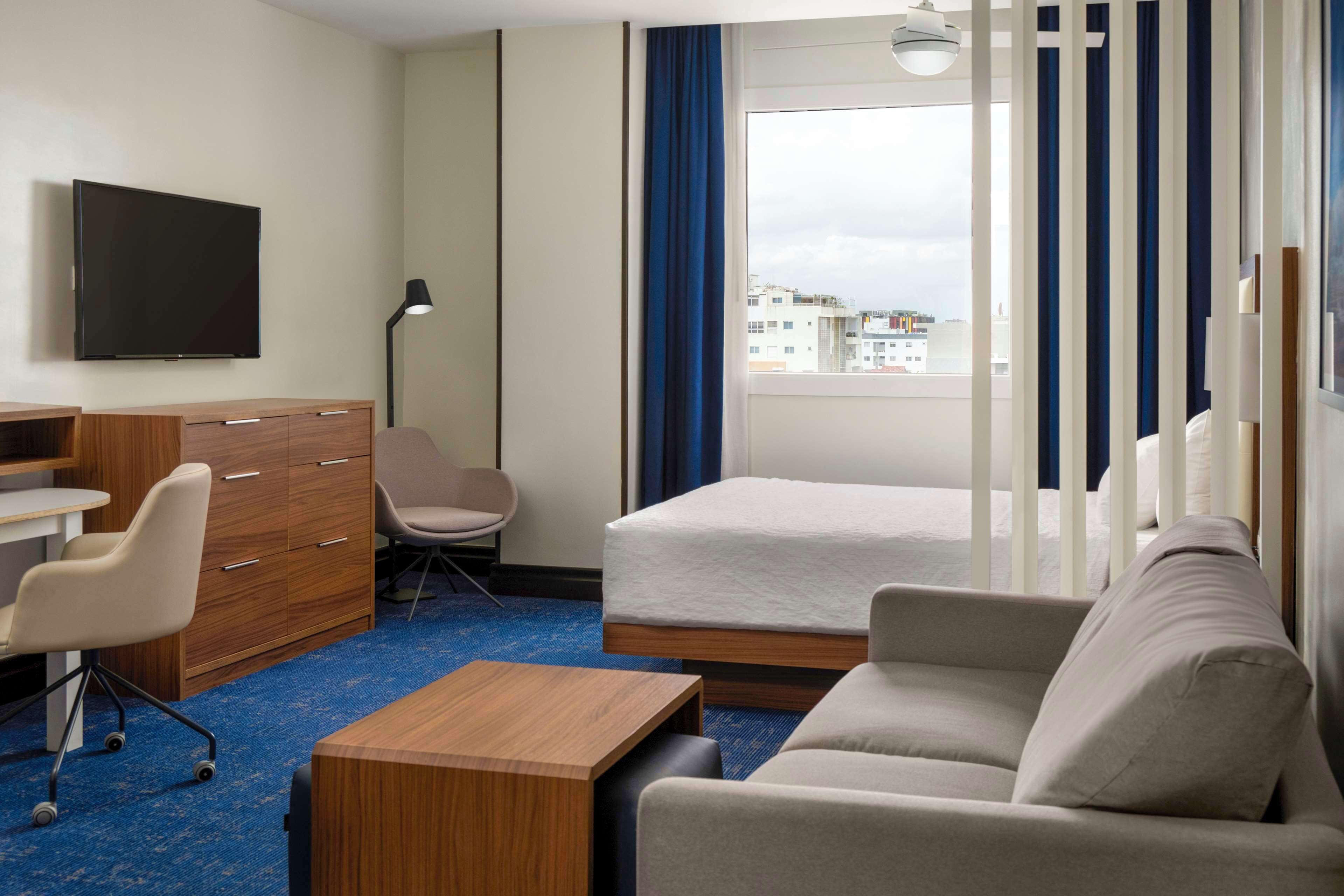 Habitació d'hotel amb un llit, una taula de treball, una cadira, un armari i una televisió.