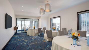 Un salón de conferencias de hotel con mesas redondas, sillas y un amplio ventanal con vista a la ciudad.