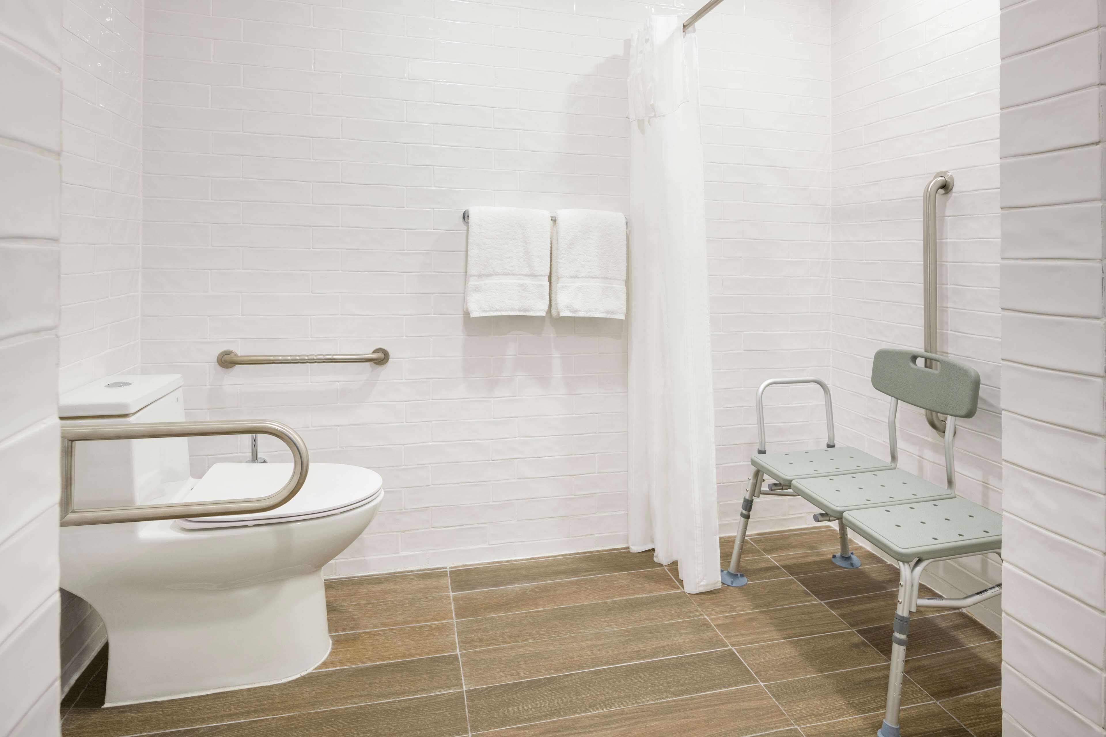 A bathroom with a white toilet, a shower with a curtain, and a grab bar.