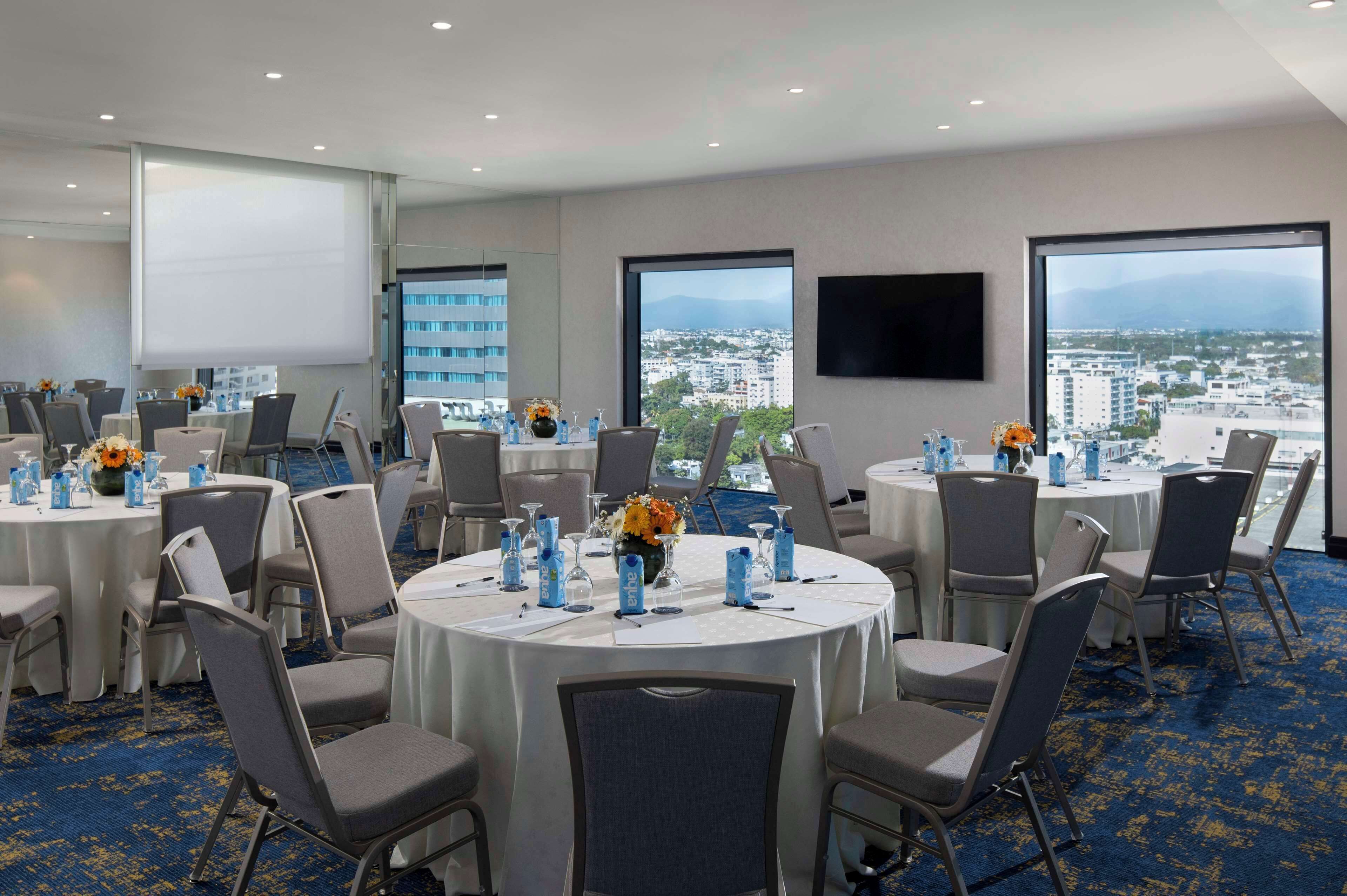 Un salón de conferencias con varias mesas, sillas y una pantalla grande.