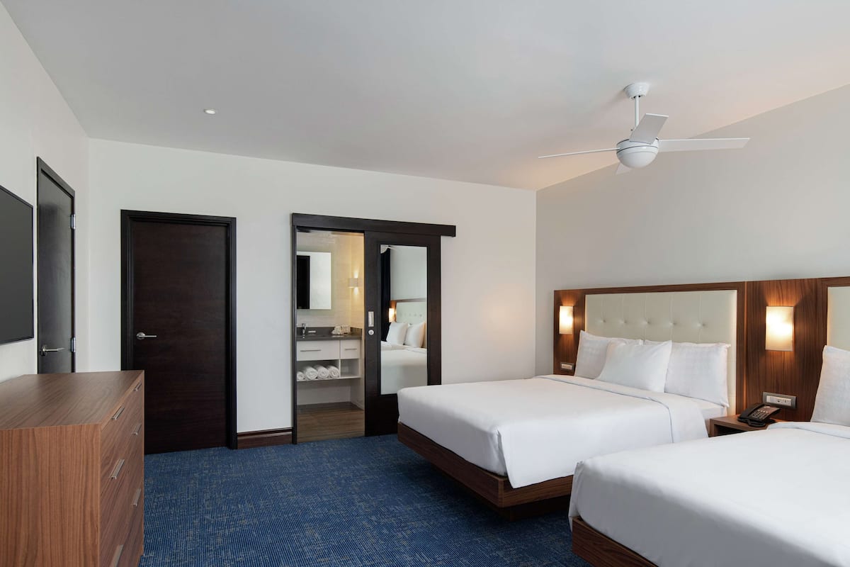 Ein Hotelzimmer mit zwei Betten, einem Kleiderschrank, einem Spiegel und einem Deckenventilator.
