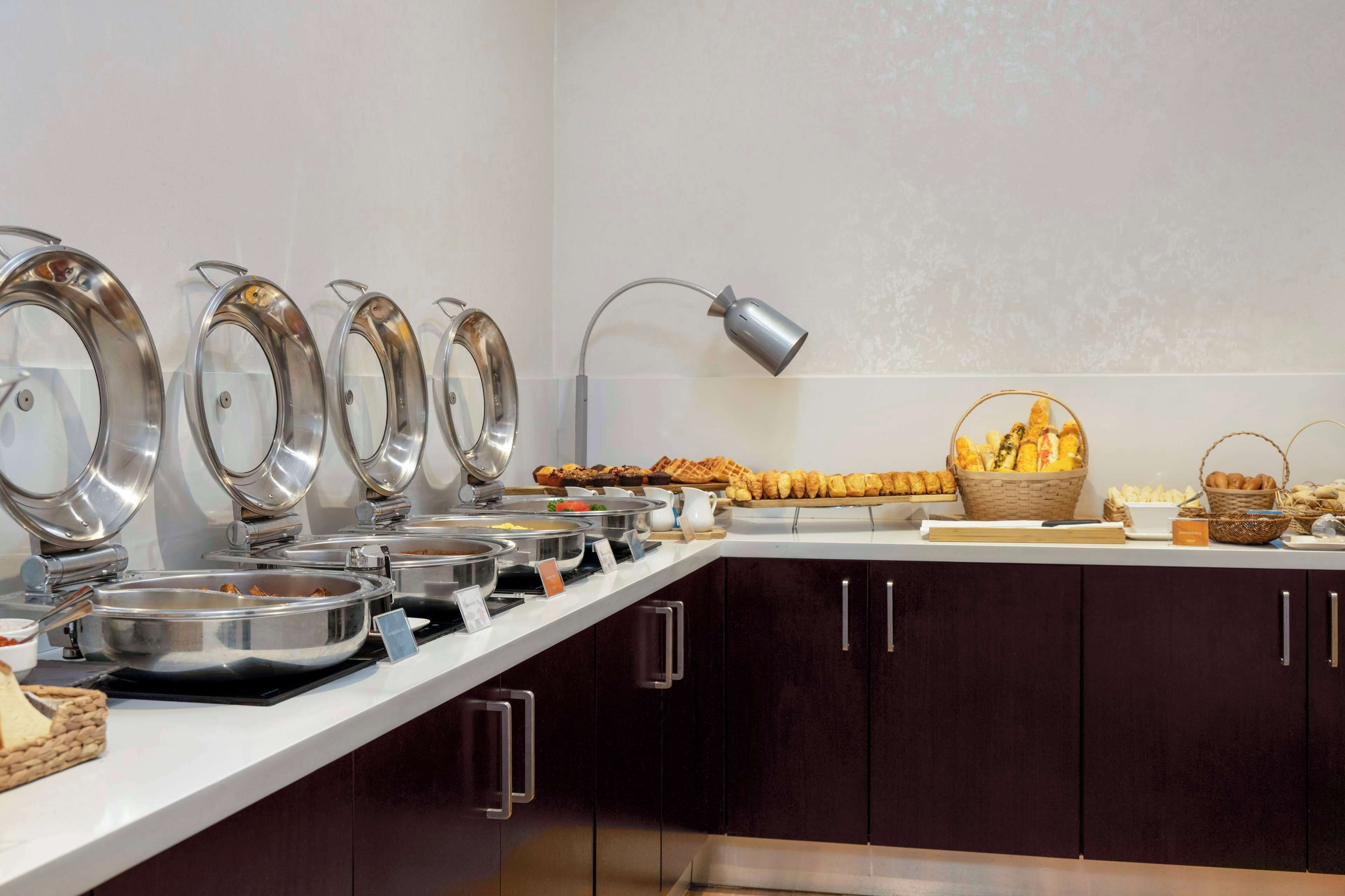 A buffet setup with multiple serving stations, a lamp, and baskets of bread and pastries.
