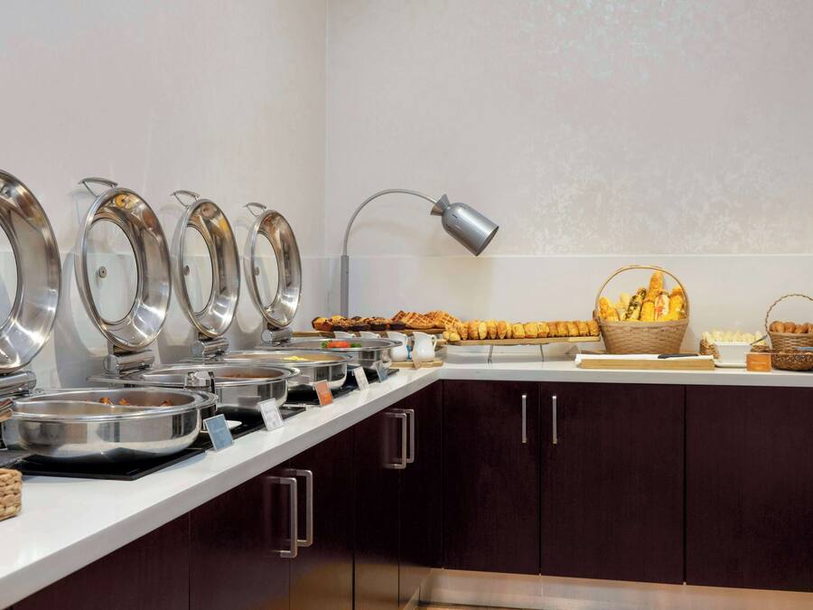 A buffet setup with multiple serving stations, a lamp, and baskets of bread and pastries.