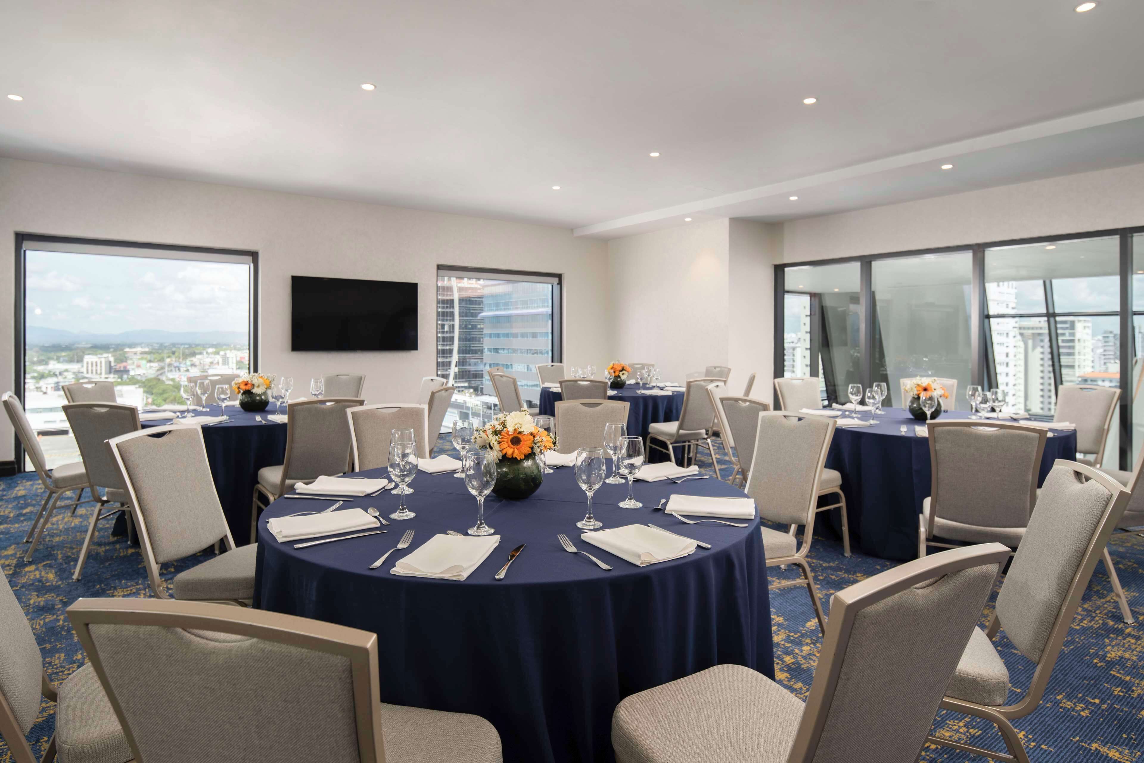 Un salón de conferencias con mesas redondas, sillas y un amplio ventanal con vista a la ciudad.