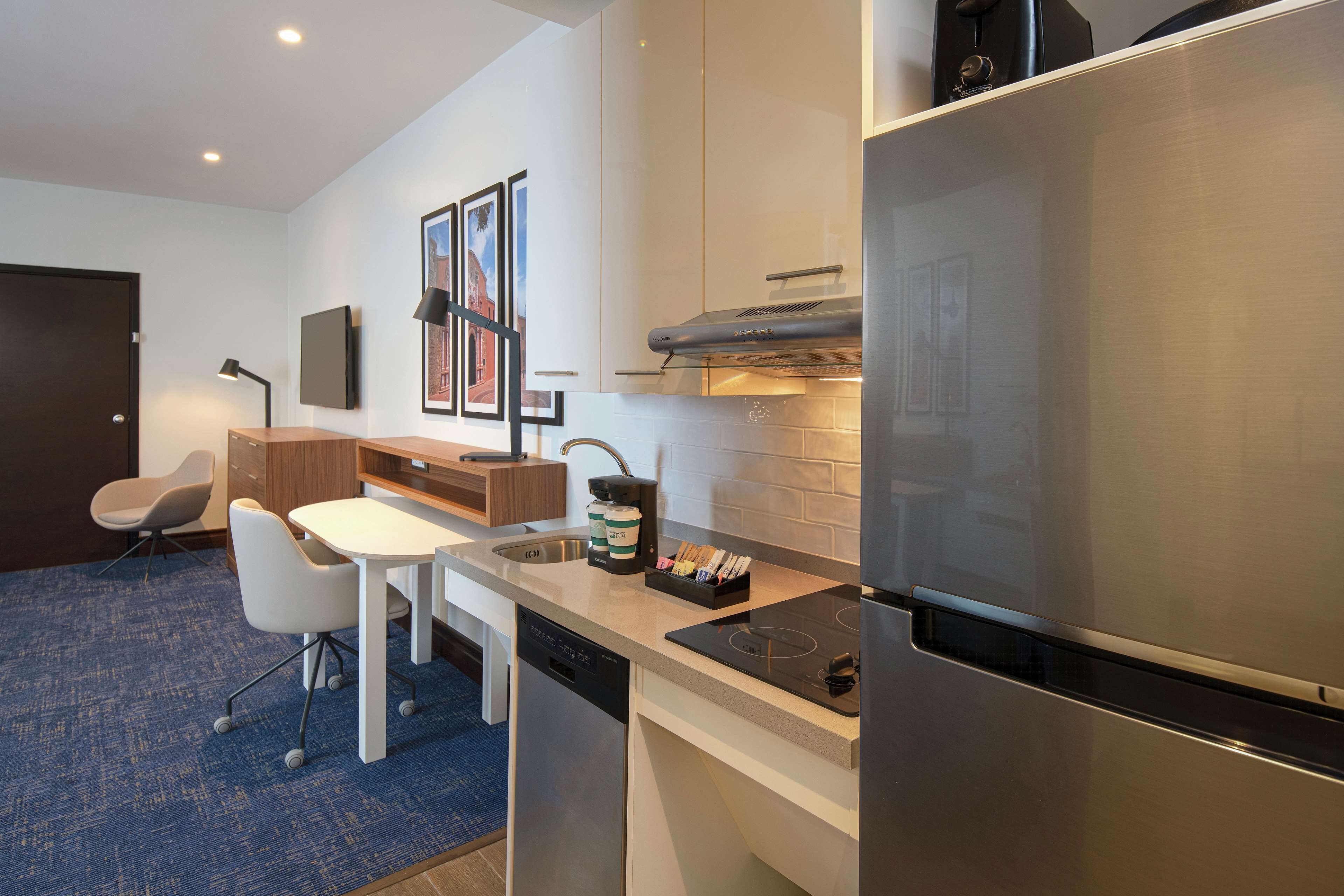 A modern kitchen with a stainless steel refrigerator, a built-in oven, and a dishwasher. There is a small dining area with a white table and two chairs.