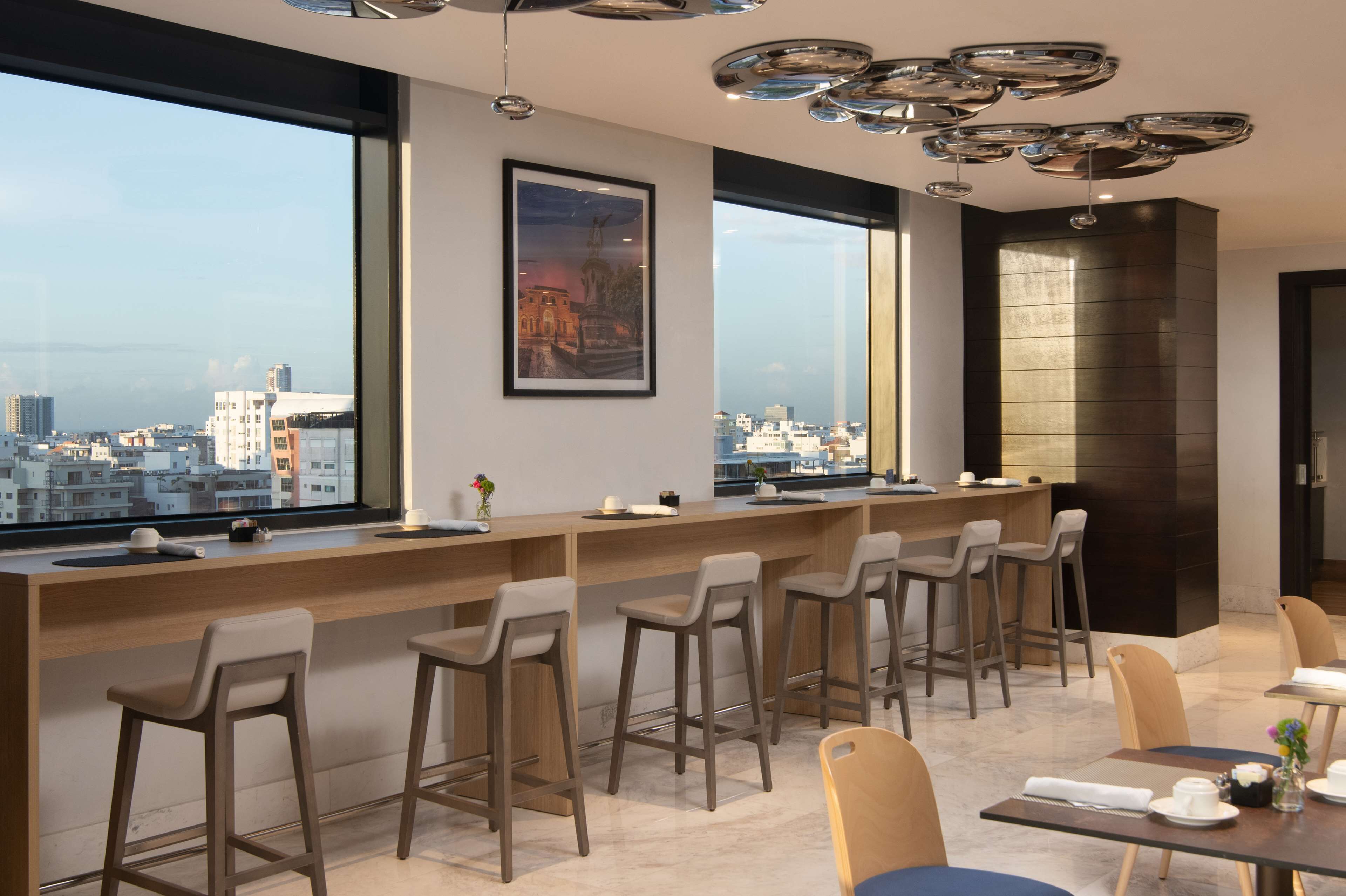 Zona de bar moderna con vista a la ciudad, taburetes y un techo alto con una lámpara de diseño único.