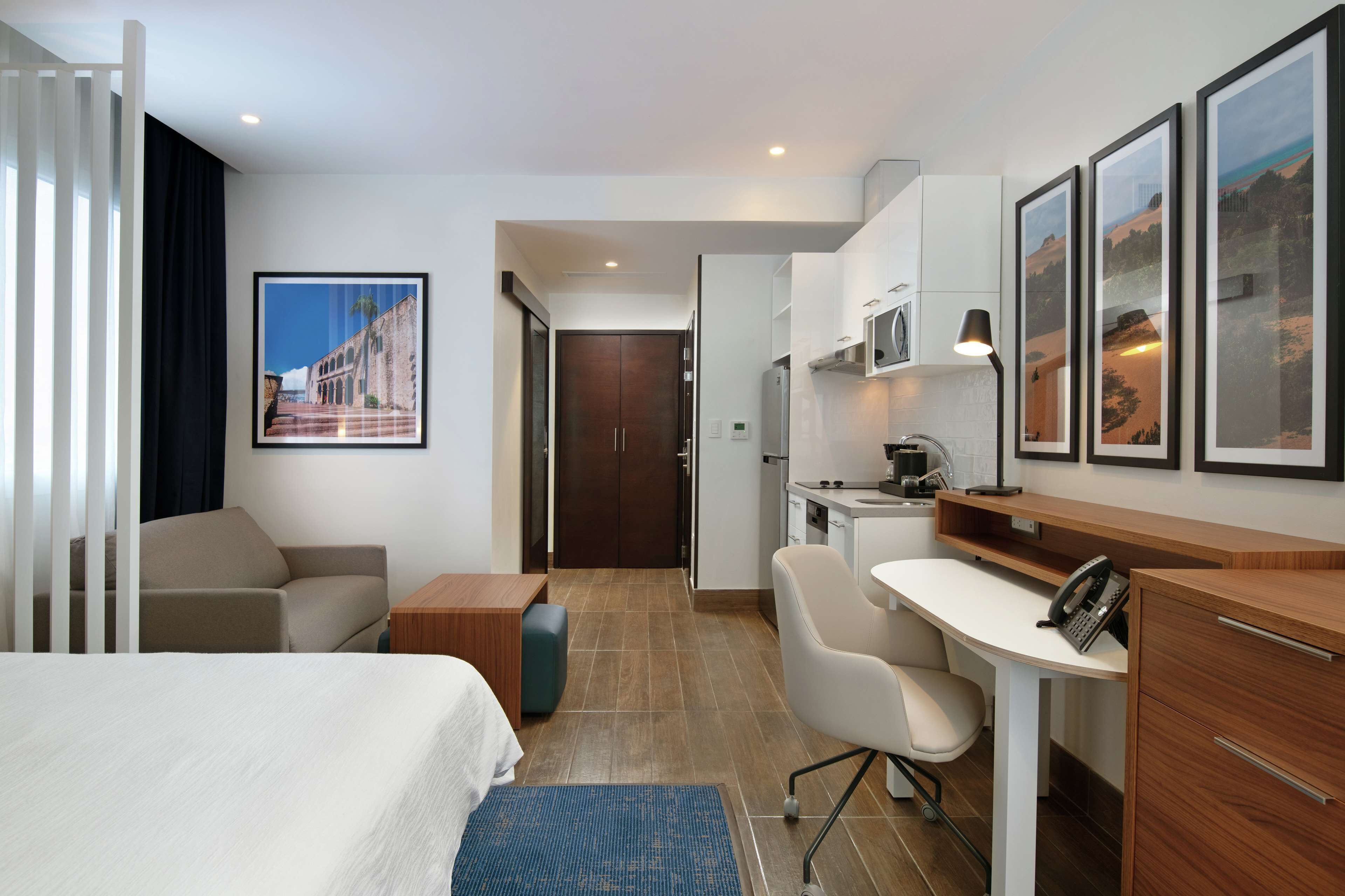 A hotel room with a bed, a desk, a chair, a small table, and a kitchenette.
