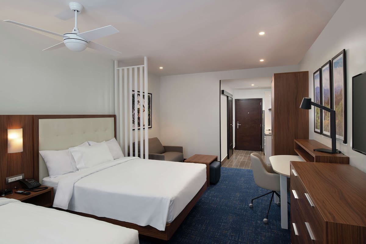Ein Hotelzimmer mit Bett, Nachttisch, Lampe, Schreibtisch, Stuhl und Fernseher.