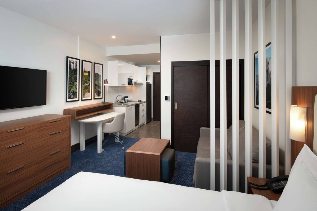 Ein Hotelzimmer mit Bett, Schreibtisch, Küchenzeile und Fernseher.