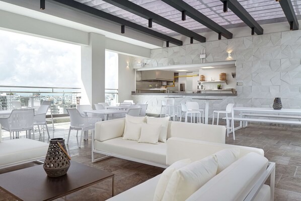 A modern living area with a sofa, dining chairs, and a kitchen in the background. - Homewood Suites by Hilton Santo Domingo, Dominican Republic (Santo Domingo)