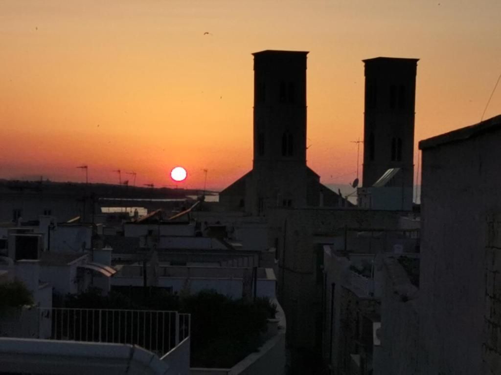 Un coucher de soleil avec deux tours imposantes se détachant sur le ciel, un pont en arrière-plan et un quartier résidentiel avec des immeubles.