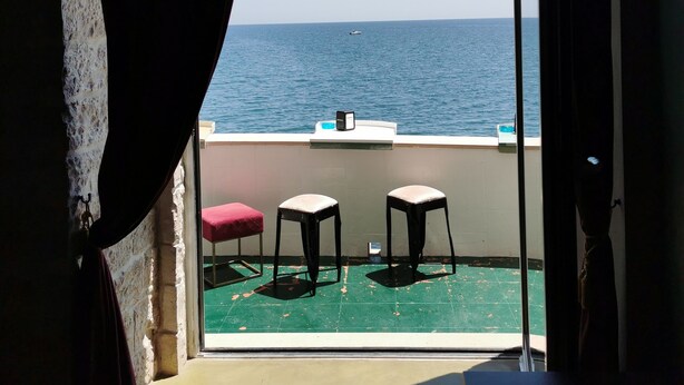 Un balcón con dos taburetes y un cojín rojo, con vista a un mar tranquilo.
