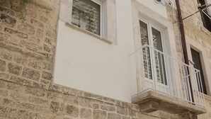 Un edificio de varios pisos con fachada de piedra, una puerta de madera y un pequeño balcón con barandilla blanca.