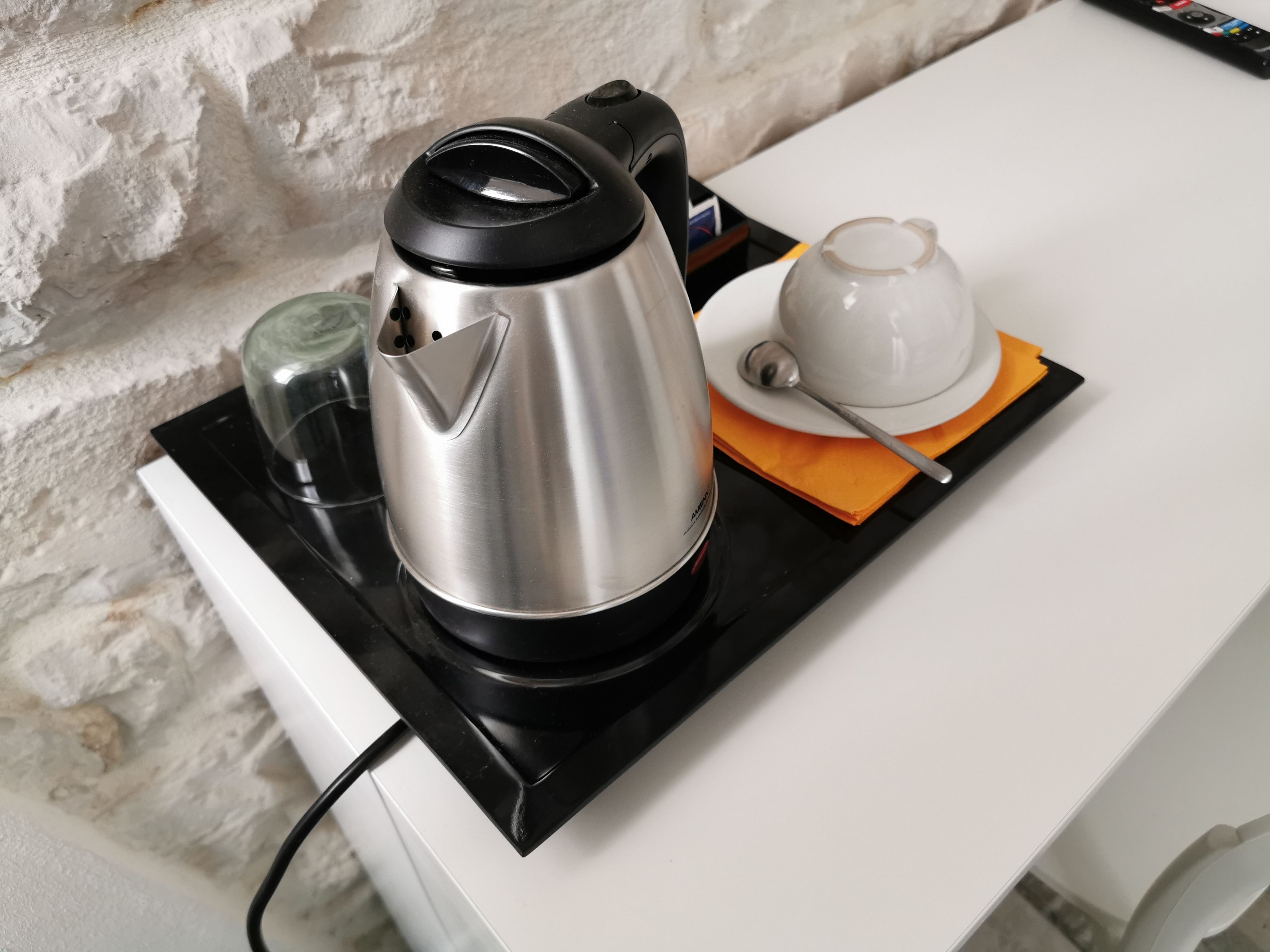 A kitchen area with a coffee maker on a black tray, a white mug, and a spoon on a white countertop.