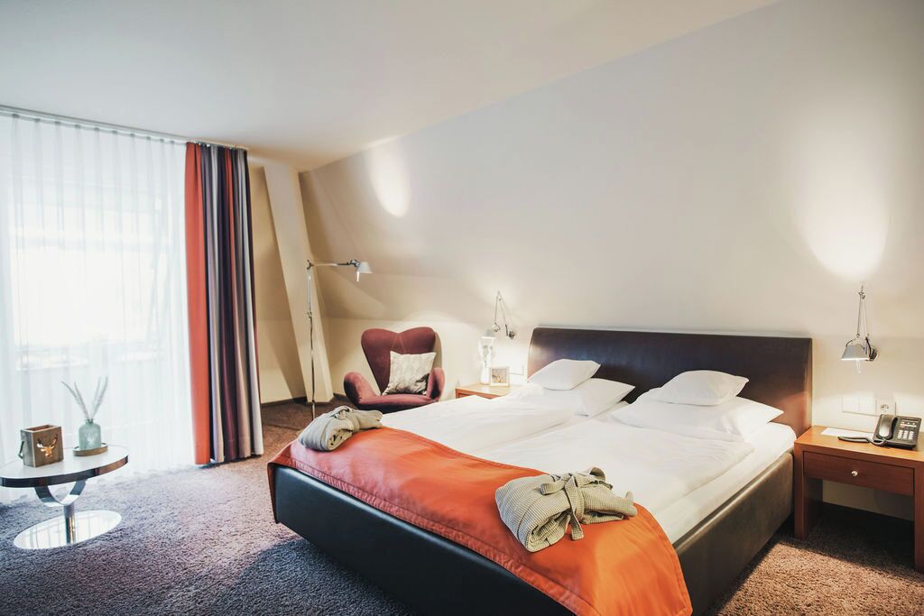 Una habitación de hotel con una cama grande, una silla, una mesita de noche y una lámpara.