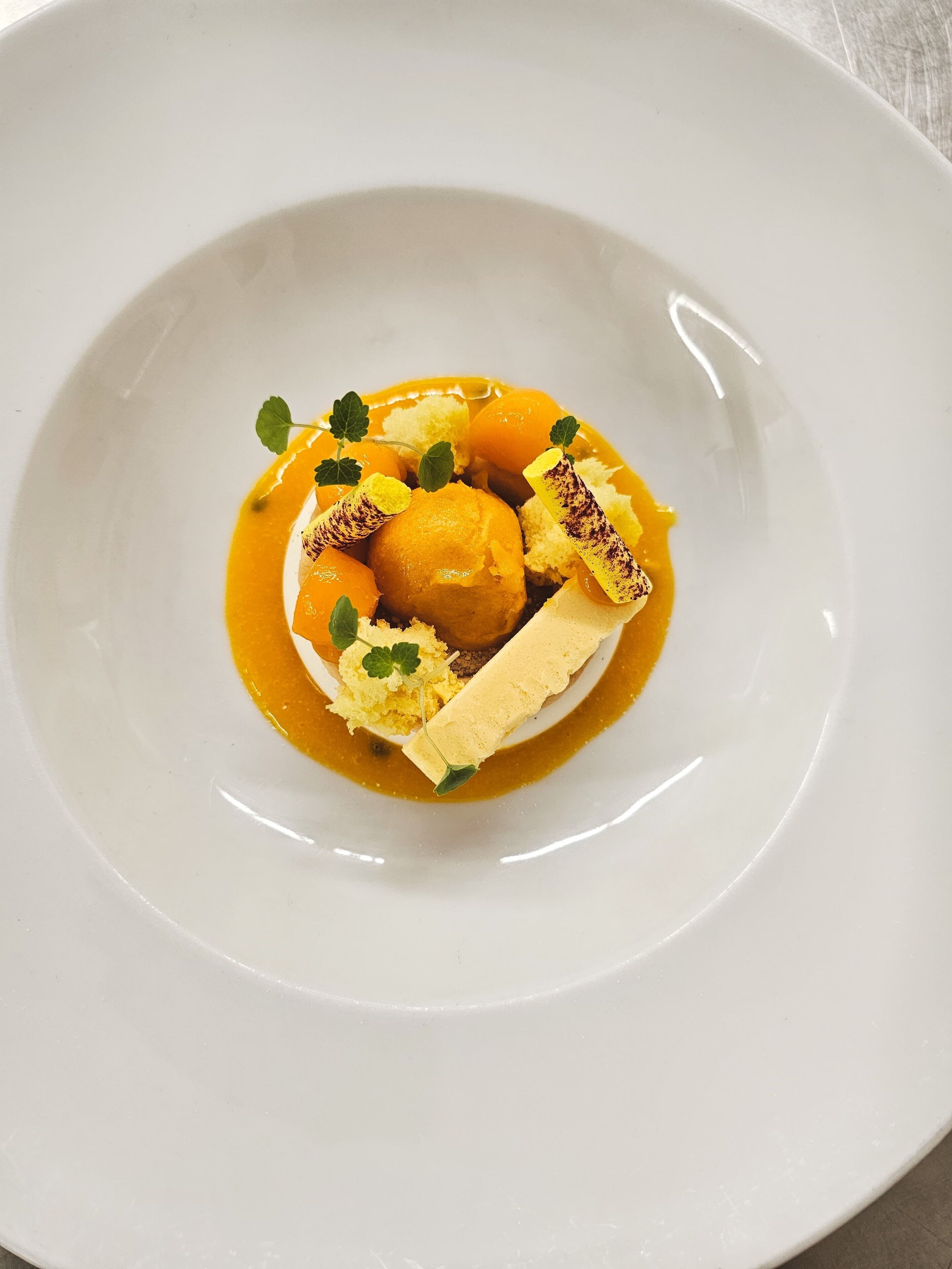Un plato blanco con un postre que incluye una bola de helado, un trozo de pastel y salsa de caramelo.