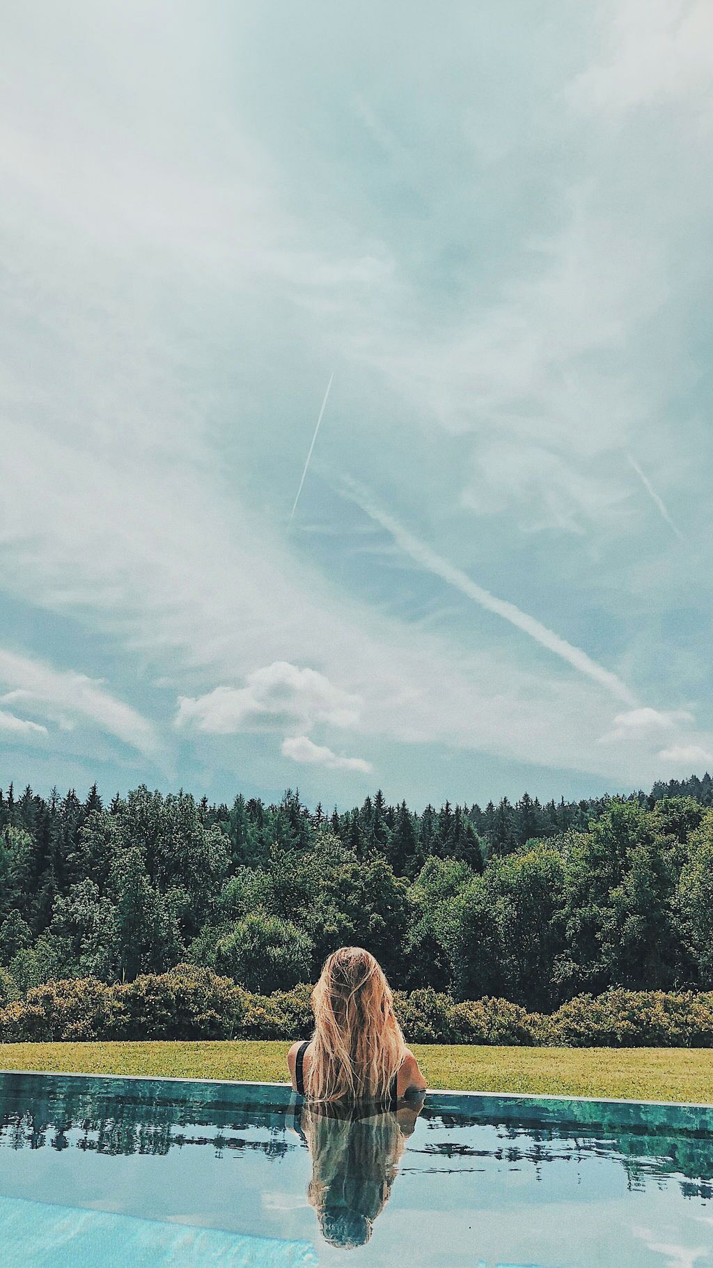 Eine Person sitzt am Pool, im Hintergrund ein Wald.