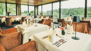 A restaurant with multiple tables set for dining, featuring white tablecloths and brown chairs. - Hotel Lauterbad (Freudenstadt)