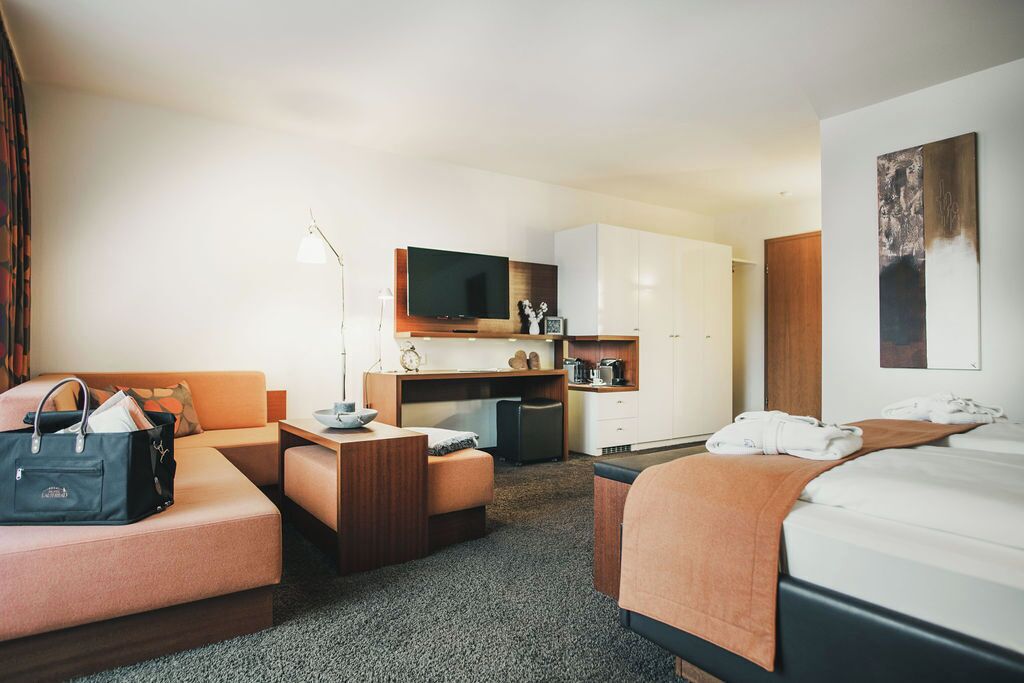 A hotel room with a bed, a sofa, a desk, a television, and a kitchenette.