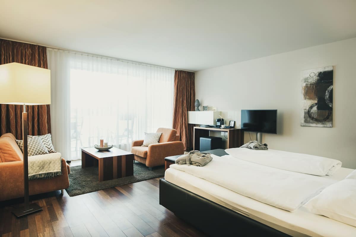 A hotel room with a bed, a sofa, a desk, a chair, and a television.