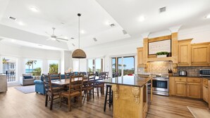 A spacious kitchen with wooden cabinets, a central island, and a dining area with a large table and chairs. - Welcome to Sea La Vie! (St. George Island)