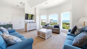 A spacious living room with a large window, a flat-screen TV, and a view of the ocean. - Welcome to Sea La Vie! (St. George Island)