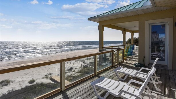 Une terrasse en bois avec des chaises longues blanches donnant sur une plage.