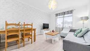 A modern living room with a dining table, wooden chairs, a grey sofa, a TV, and a lamp. - Two Bedroom Apartment by Klass Living Serviced Accommodation Motherwell - Anderson Apartment With WiFi &Parking (Motherwell)