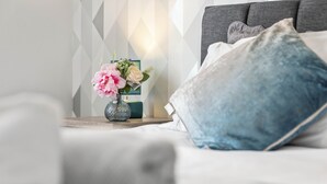 A neatly made bed with a blue pillow, a vase with pink flowers, and a geometric-patterned wall. - Two Bedroom Apartment by Klass Living Serviced Accommodation Motherwell - Anderson Apartment With WiFi &Parking (Motherwell)