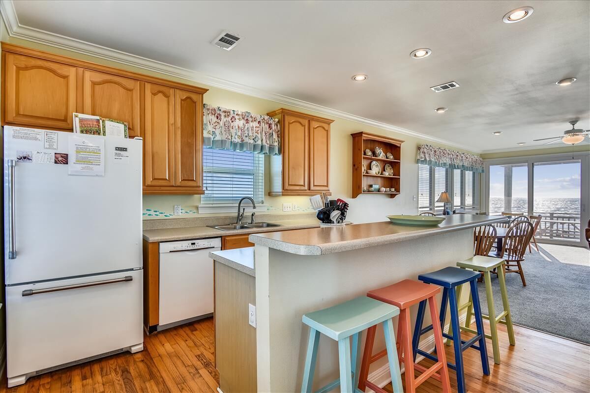 A kitchen with wooden cabinets, a refrigerator, a sink, and a bar area with stools.