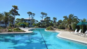 A swimming pool with lounge chairs and umbrellas, surrounded by palm trees and a building in the background. - TRADEWINDS HAS LONG BEEN praised as a uniquely appointed home where treasured memories are made. (St. George Island)