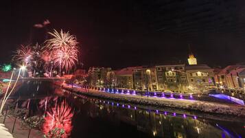 A nighttime view of a riverside area with fireworks, illuminated buildings, and a bridge.