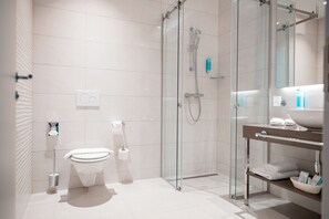 Un baño moderno con cabina de ducha de vidrio, inodoro y tocador con espejo y lavamanos.