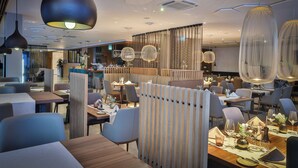 A modern restaurant interior with high tables, comfortable seating, and stylish pendant lighting. - Hotel Seven (Villach)