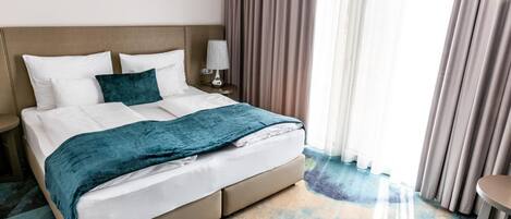 A hotel room with a bed, nightstand, lamp, and curtains.
