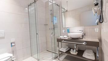 Un baño moderno con ducha envuelta en vidrio, un lavamanos amplio y un tocador con toallas y artículos de aseo.