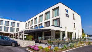 A hotel with a modern design, featuring a café-bar on the ground floor, outdoor seating, and a well-maintained garden area. - Hotel Seven (Villach)