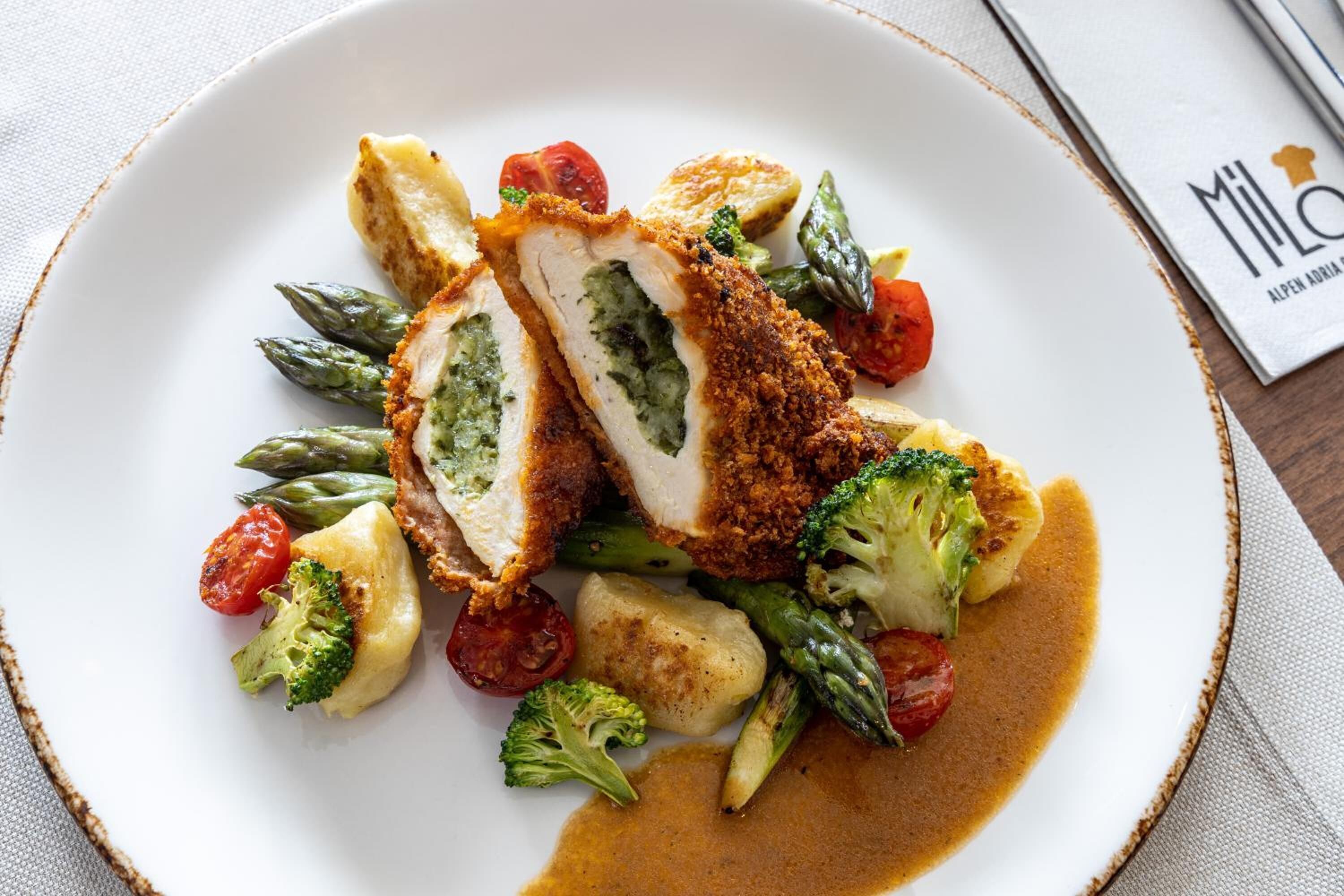 Een bord eten met een gepaneerde kip schnitzel, asperges, kerstomaatjes en aardappelen.
