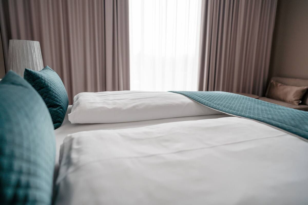 A hotel room with a bed, pillows, and curtains.