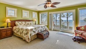 A bedroom with a bed, two bedside lamps, a ceiling fan, and a view of the ocean through a sliding glass door.