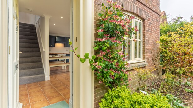 A brick house with a staircase leading to an interior, a window with pink flowers, and a green door mat.