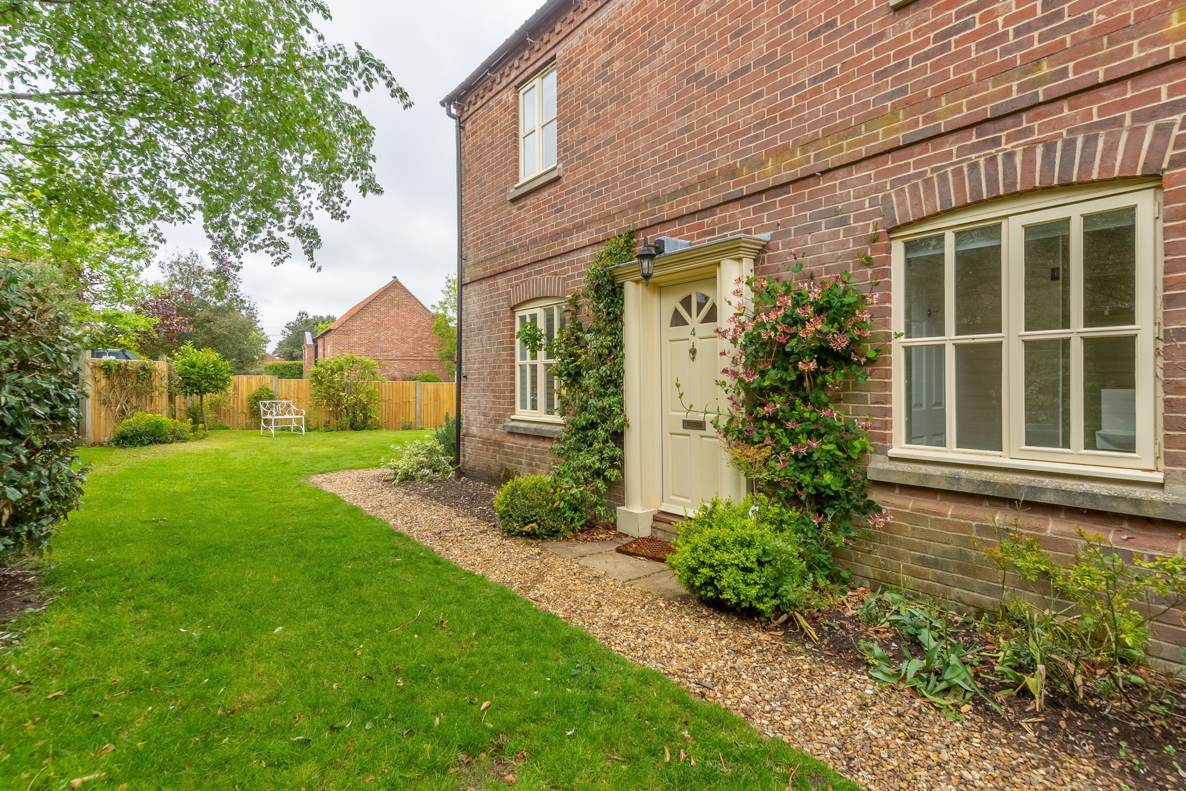 A brick house with a well-maintained garden, a white door, and a window with a white frame.